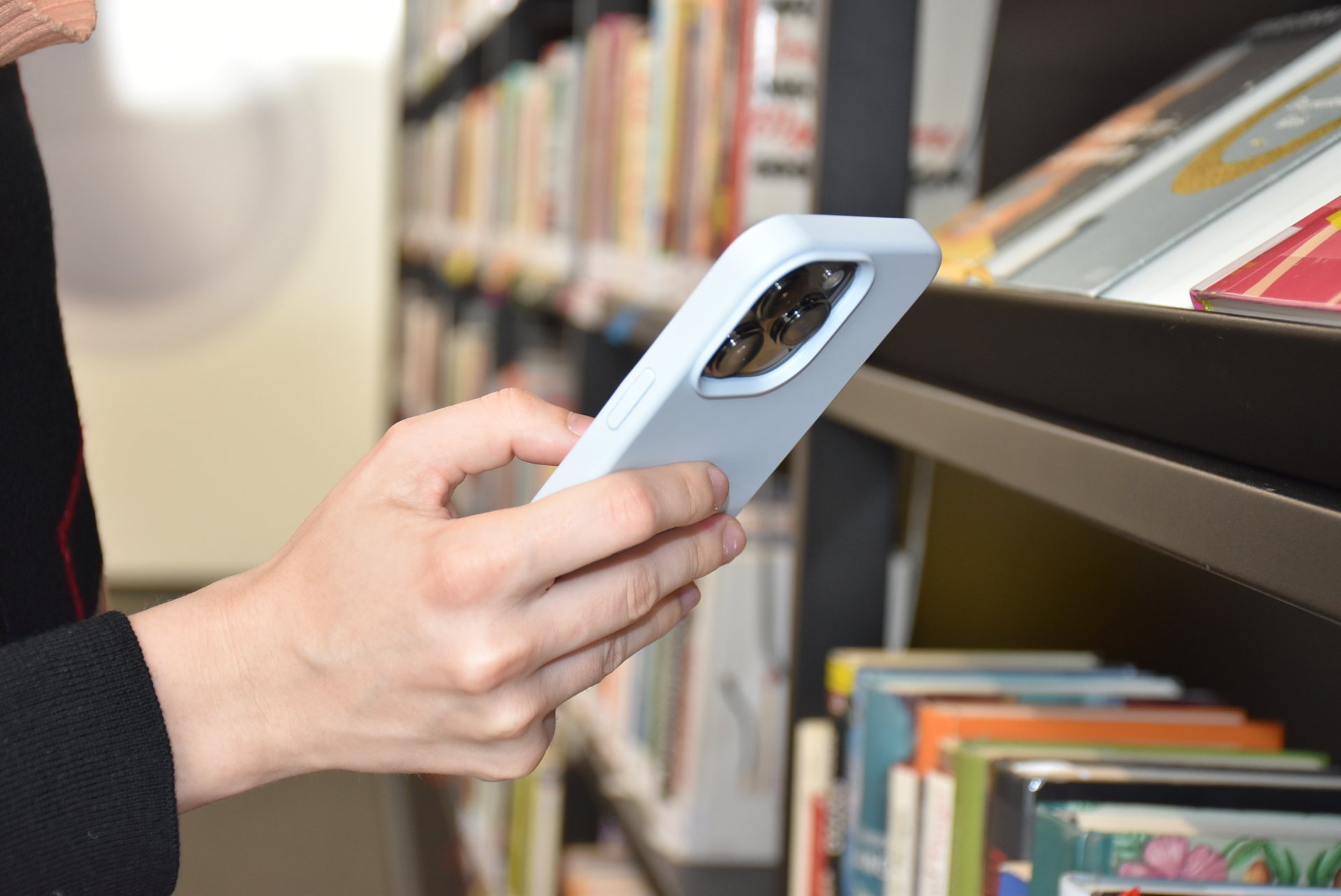 Hand mit Handy vor Bibliotheksregal
