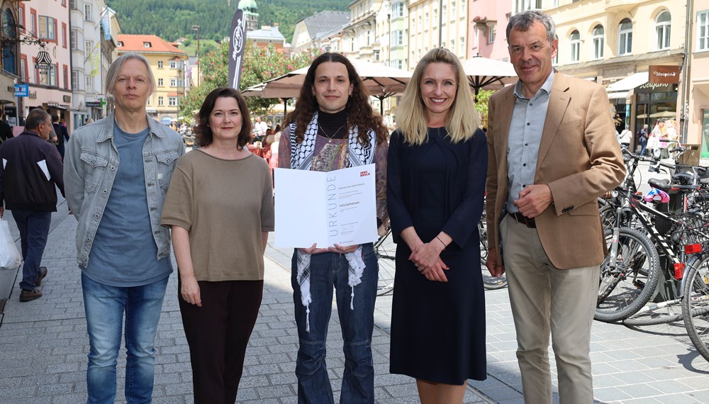 Im Bild stehen fünf lächelnde Menschen in der Maria-Theresienstrage: Andrei Siclodi (Direktor künstler*innenhaus Büchsenhausen), Natalie Pedevilla (Referat Bildende Kunst und Kulturprojekte), Innsbrucks Büchsenhausen-Fellow 2024 Felix Kalmenson, Kulturamtsleiterin Isabelle Brandauer und Vizebürgermeister Georg Willi. Der Innsbrucks Büchsenhausen-Fellow 2024 Felix Kalmenson hält eine Urkunde in der Hand.