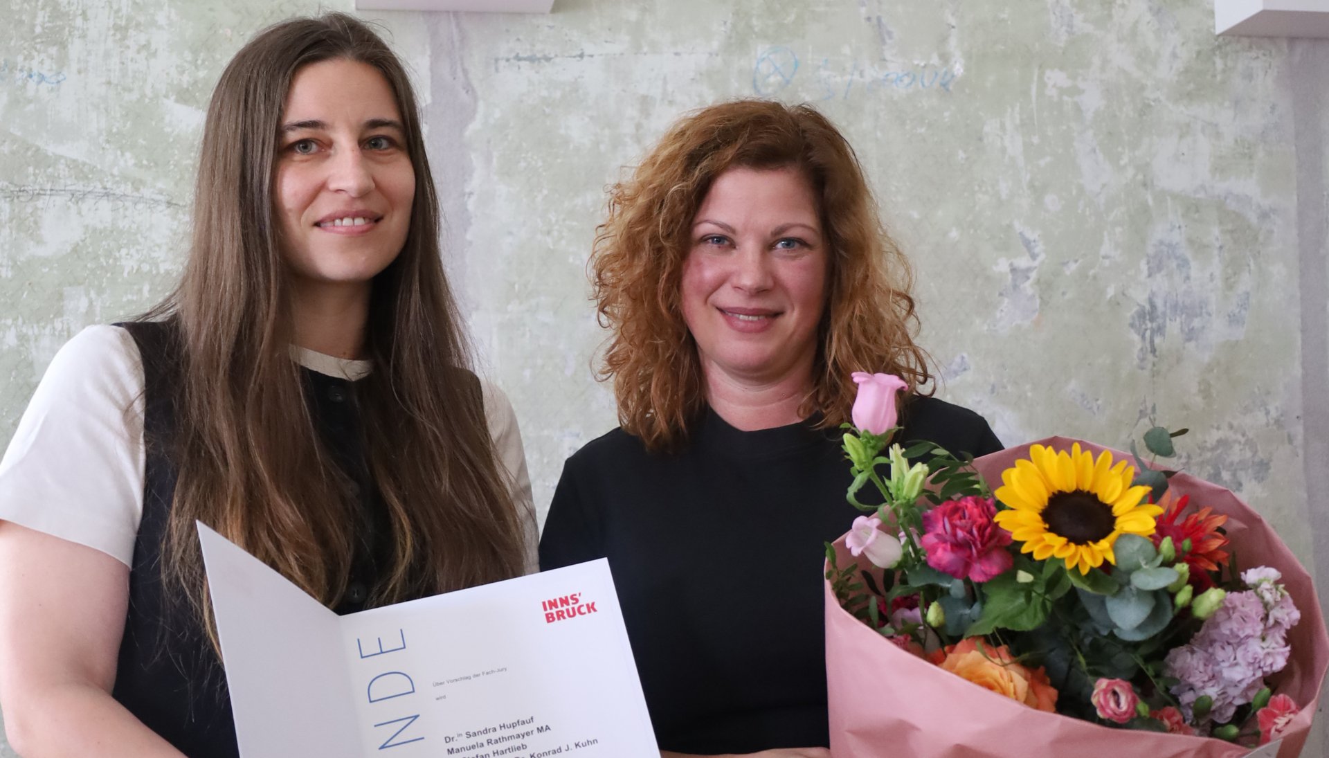 Die Preisträgerinnen der gedenk_potenziale 2026 Manuela Rathmayer mit der Urkunde in Händen und Sandra Hupfauf mit einem Blumenstrauß in der Hand