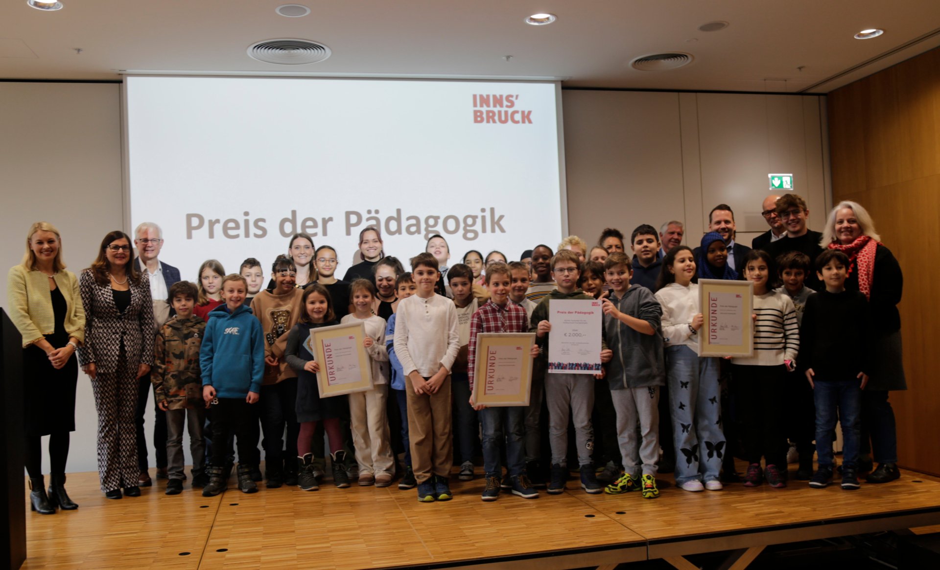 Eine Volksschulklasse mit ihren Lehrern halten Urkunden in den Händen.