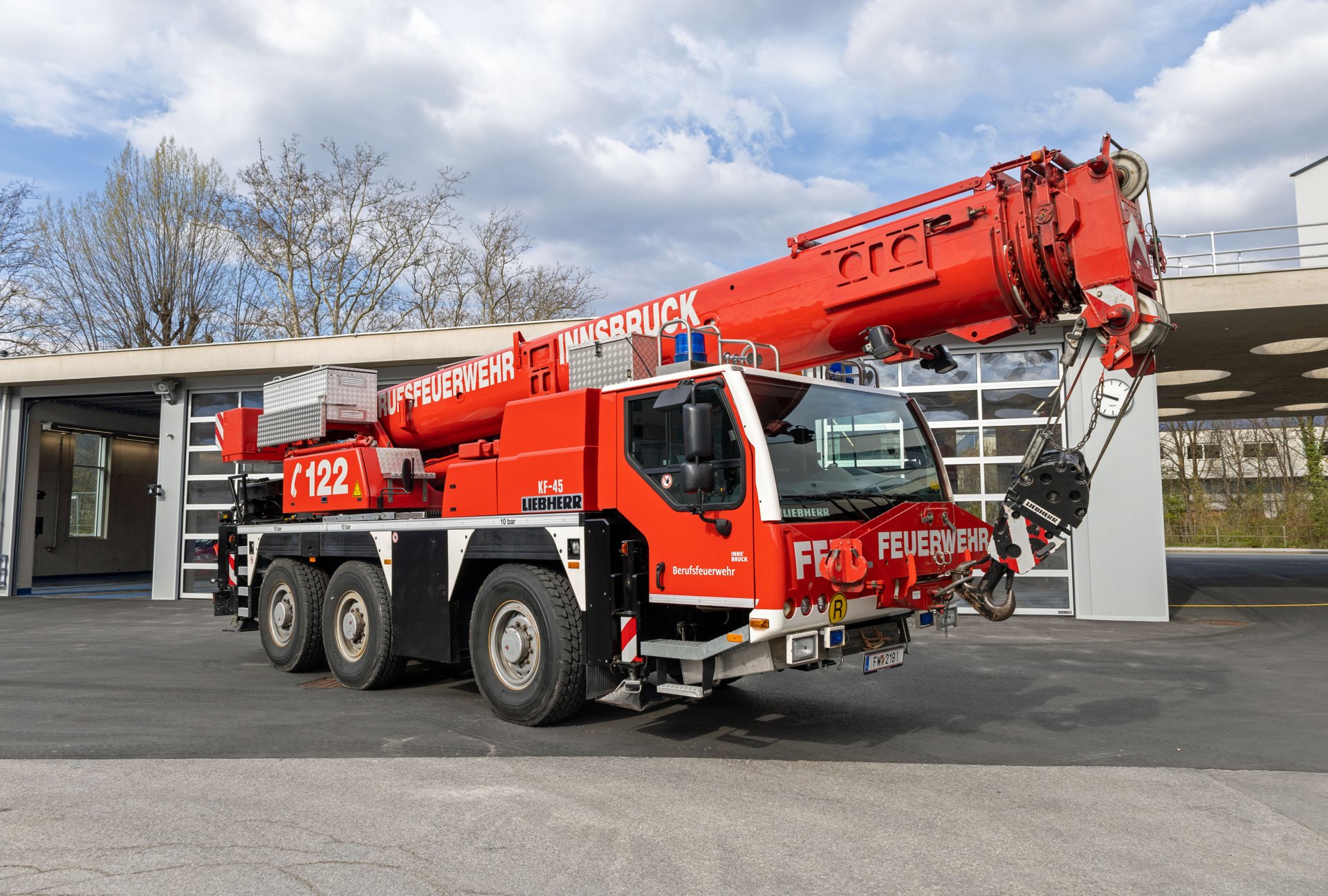 Ein rotes Kranfahrzeug steht bei Tageslicht vor dem Gebäude der Berufsfeuerwehr Innsbruck.