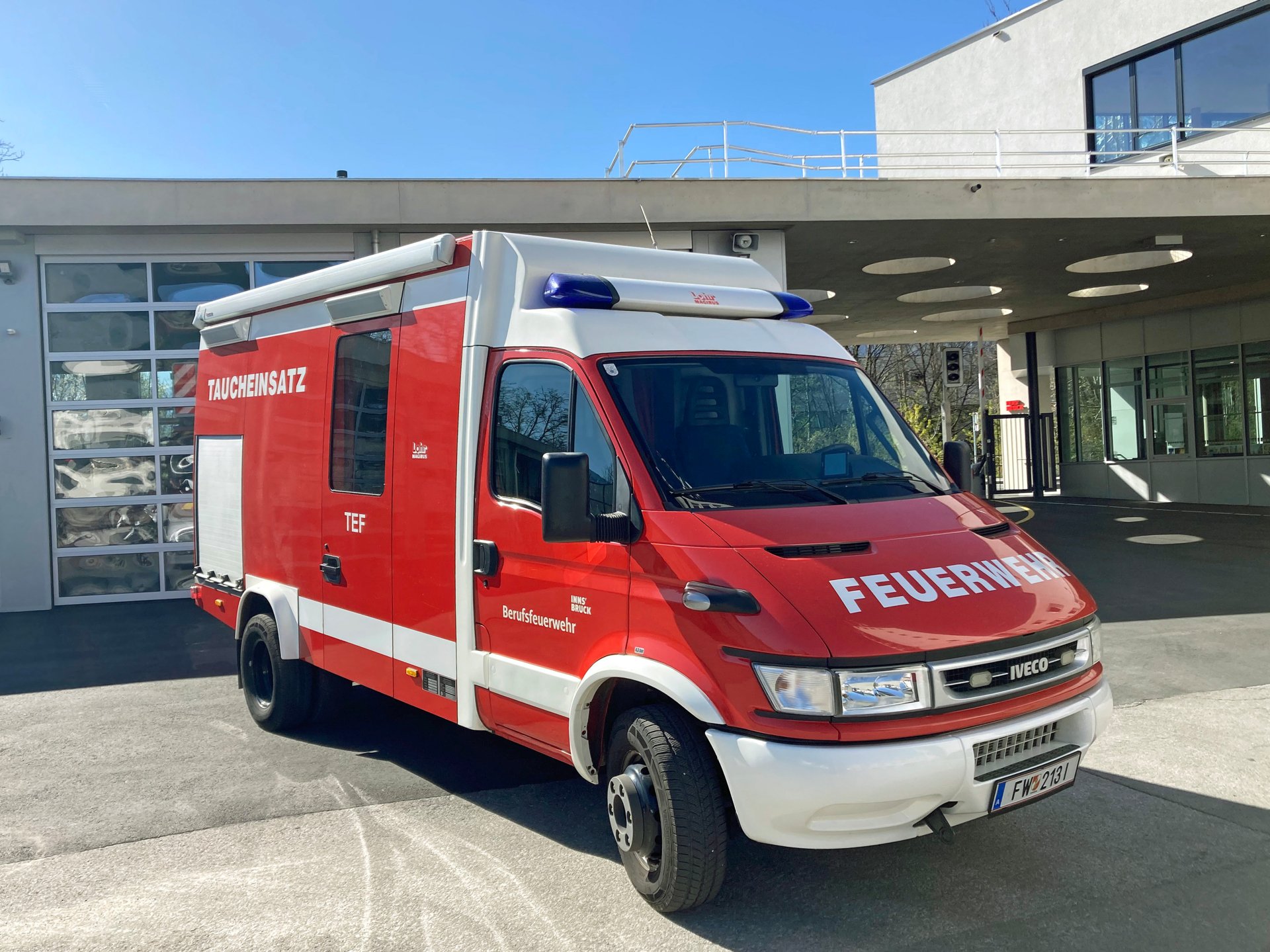 Ein rotes Taucheinsatzfahrzeug steht bei Tageslicht vor dem Gebäude der Berufsfeuerwehr Innsbruck.