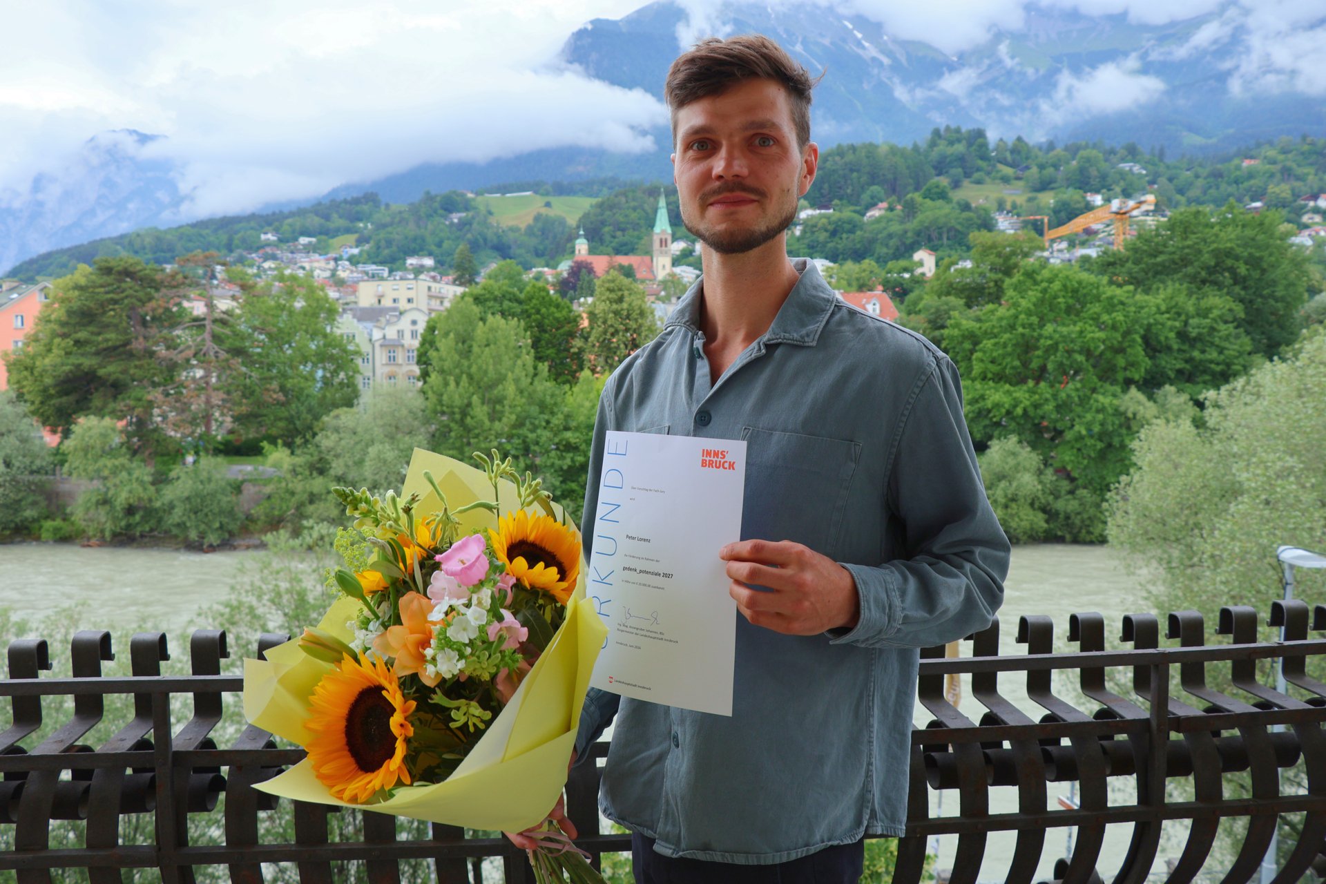Der Tiroler Autors Peter Lorenz mit einem Blumenstrauß und seiner Urkunde für das Gewinner-Projekt der gedenk_potenziale 2027 "Reisebüro Schleich".