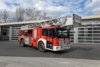 Ein rotes Fahrzeug mit Drehleiter mit Korb steht bei Tageslicht vor dem Gebäude der Berufsfeuerwehr Innsbruck.