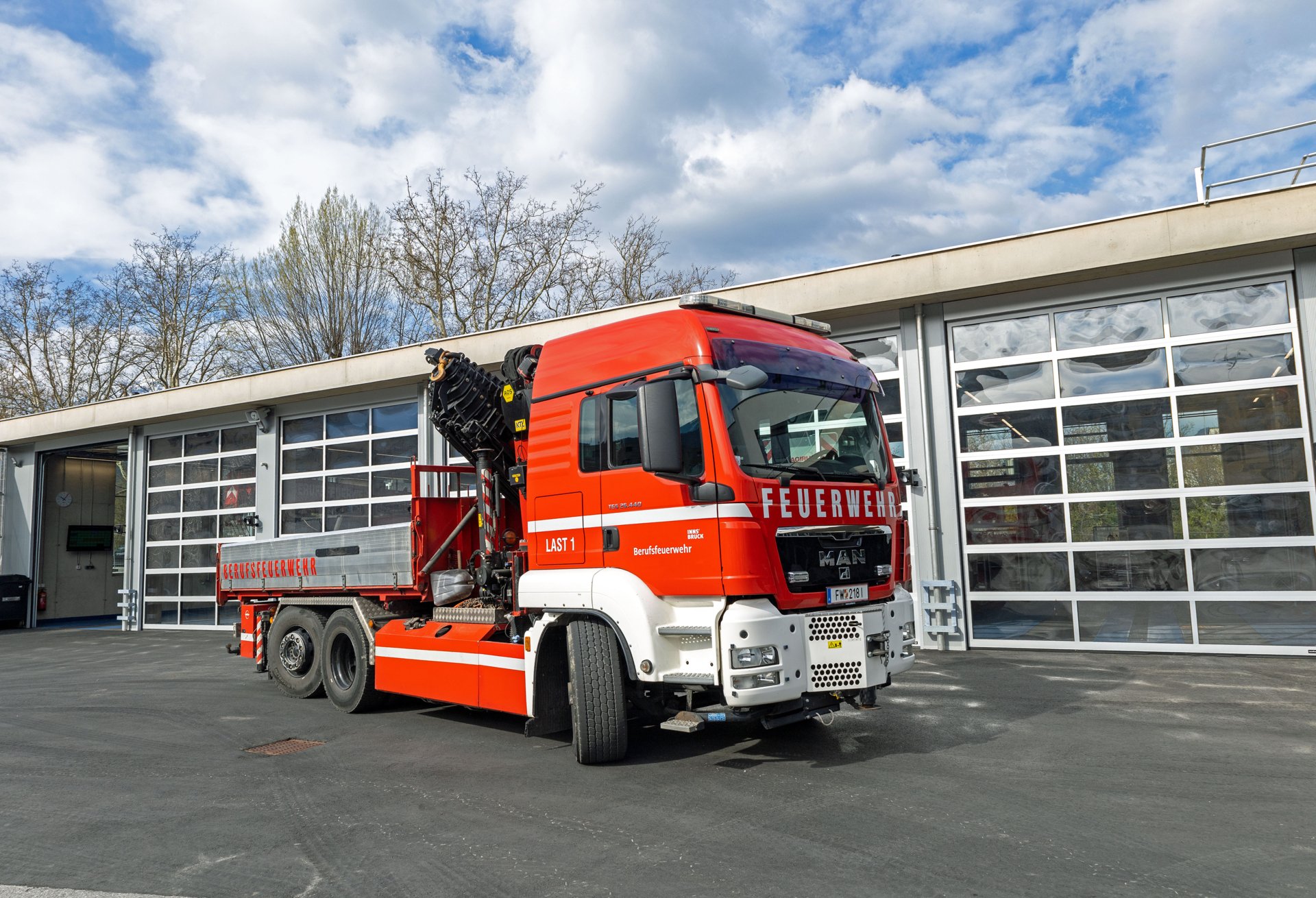 Ein roter Lastkraftwagen mit Kran steht bei Tageslicht vor dem Gebäude der Berufsfeuerwehr Innsbruck.
